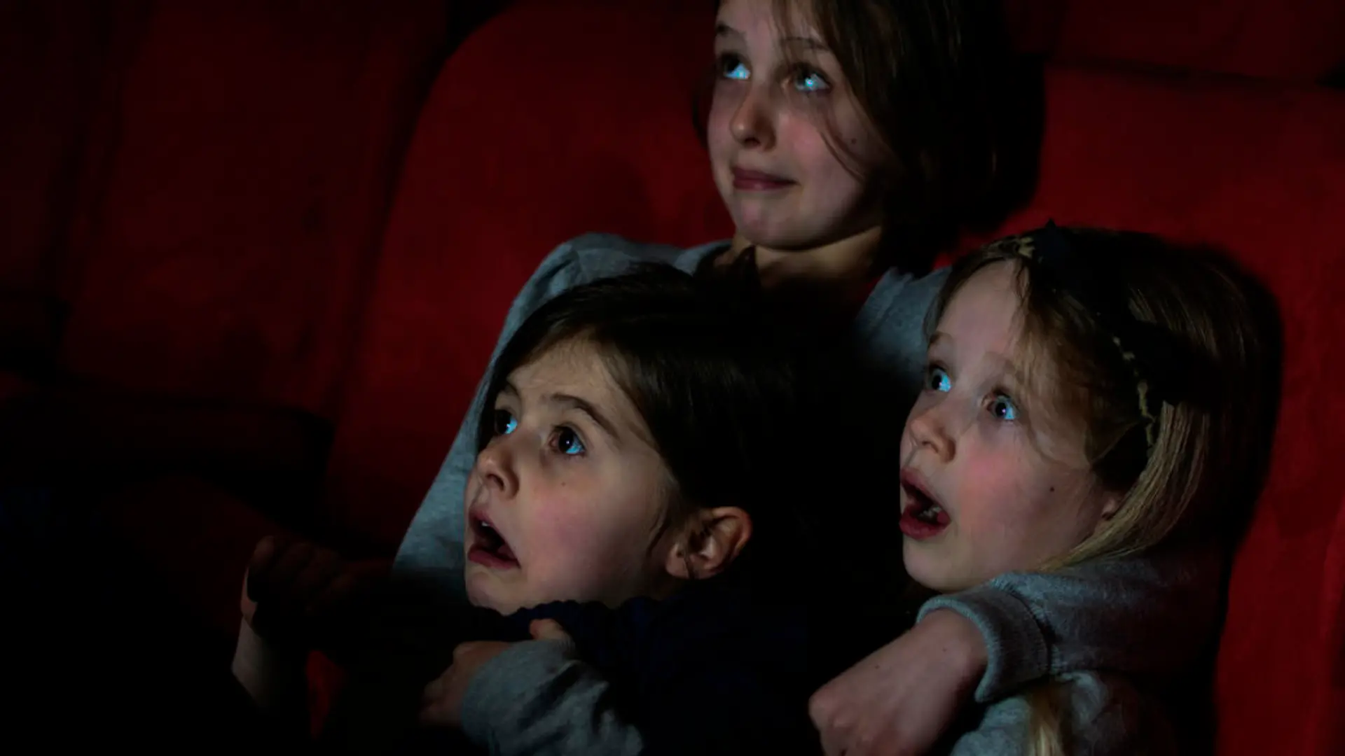 Three young girls watching a scary film moment in the cinema.