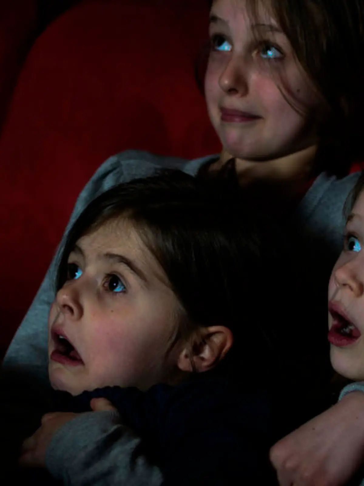 Three young girls watching a scary film moment in the cinema.