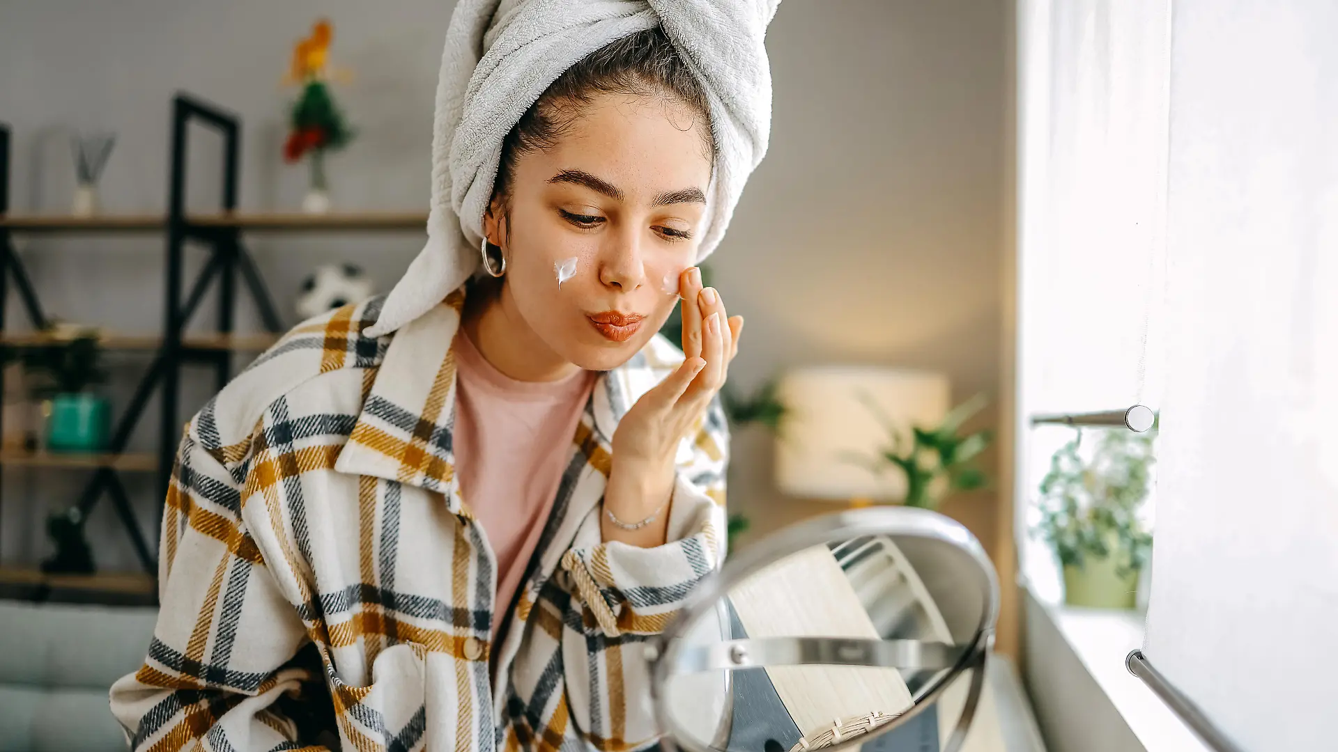 One woman, a beautiful young woman sitting in the living room applying face cream, has a towel on her head.