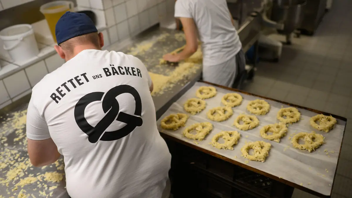 08.09.2022, Niedersachsen, Hannover: Ein Bäcker und eine Auszubildende stehen am frühen Morgen mit einem T-Shirt ·Rettet uns Bäcker· in der Backstube der Bäckerei Fahrenhorst. Die norddeutschen Innungsbäckereien machen am 08. September mit der Aktion ·Uns geht das Licht aus · Heute das Licht und morgen der Ofen?· auf gestiegene Energiekosten aufmerksam, die viele Betriebe in ihrer Existenz bedrohen. Foto: Julian Stratenschulte/dpa +++ dpa-Bildfunk +++