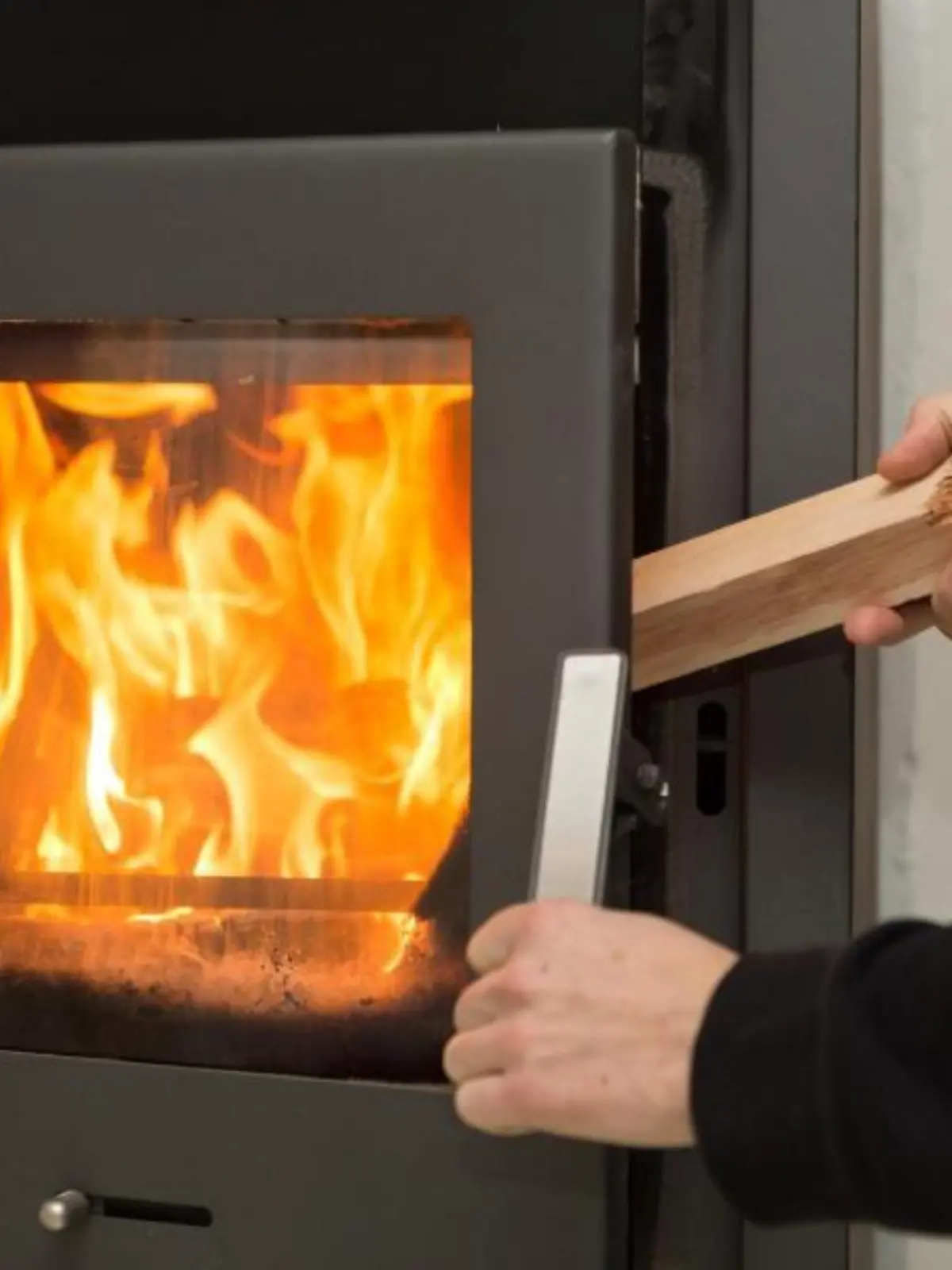 Man legt Holz in brennenden Kaminofen
