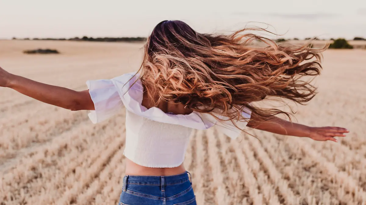 Summer Girl enjoying nature on yellow field. Beautiful young woman dancing Outdoors. Long hair in the wind. Happiness and lifestyle. Back view