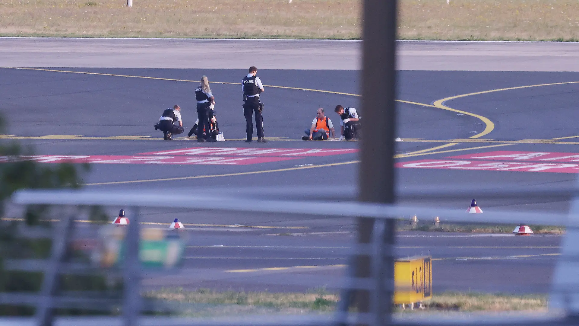 dpatopbilder - 13.07.2023, Nordrhein-Westfalen, Düsseldorf: Polizisten stehen auf dem Flugfeld und versuchen Aktivisten der Gruppe Letzte Generation am Flughafen vom Asphalt zu lösen, nachdem sie sich festgeklebt haben. Foto: David Young/dpa +++ dpa-Bildfunk +++