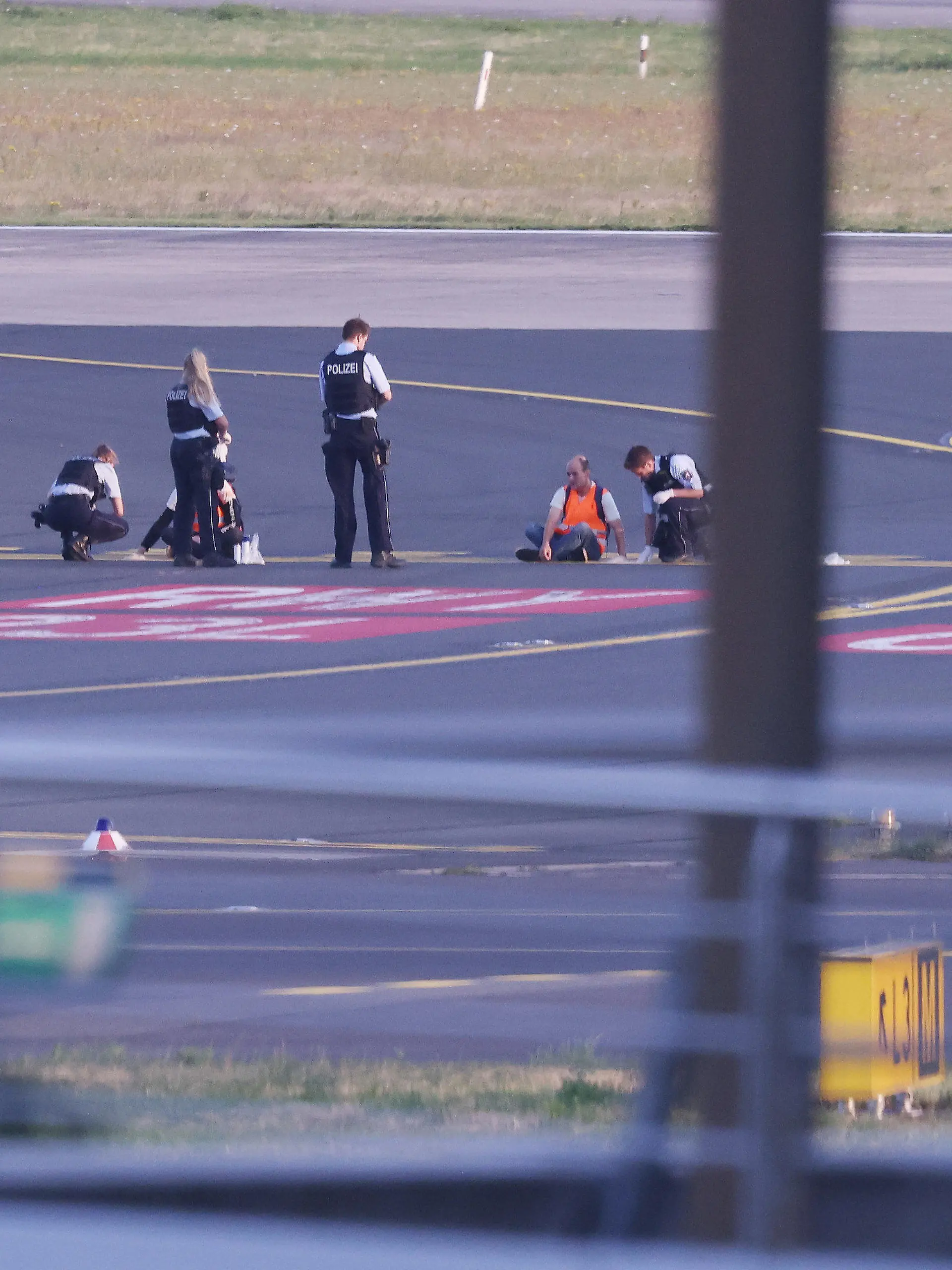 dpatopbilder - 13.07.2023, Nordrhein-Westfalen, Düsseldorf: Polizisten stehen auf dem Flugfeld und versuchen Aktivisten der Gruppe Letzte Generation am Flughafen vom Asphalt zu lösen, nachdem sie sich festgeklebt haben. Foto: David Young/dpa +++ dpa-Bildfunk +++