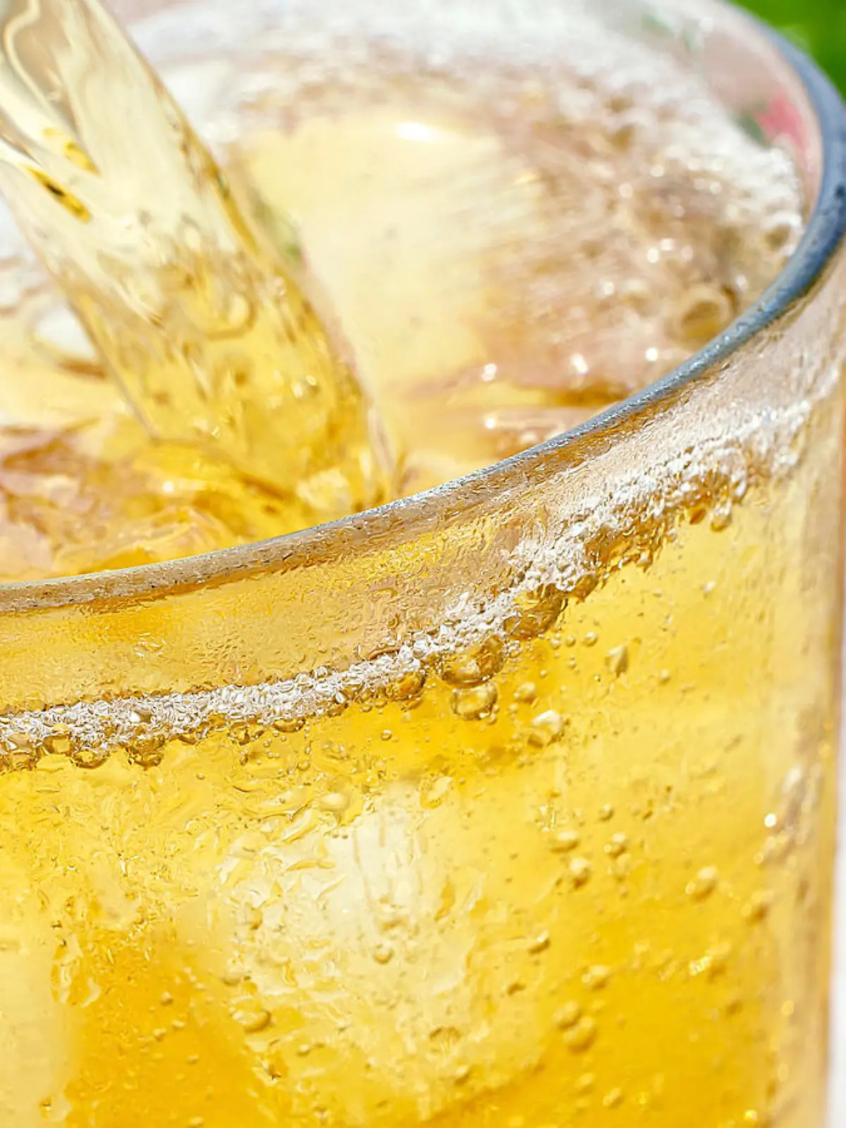 Ein Glas erfrischende eiskalte Apfelsaftschorle Apfelschorle mit Eisw?rfeln wird eingeschenkt. Das kalte Glas hat kondensierte Wassert?pfchen. Im Hintergrund ist ein Apfel und aufgeschnittene Apfelschnitze. 