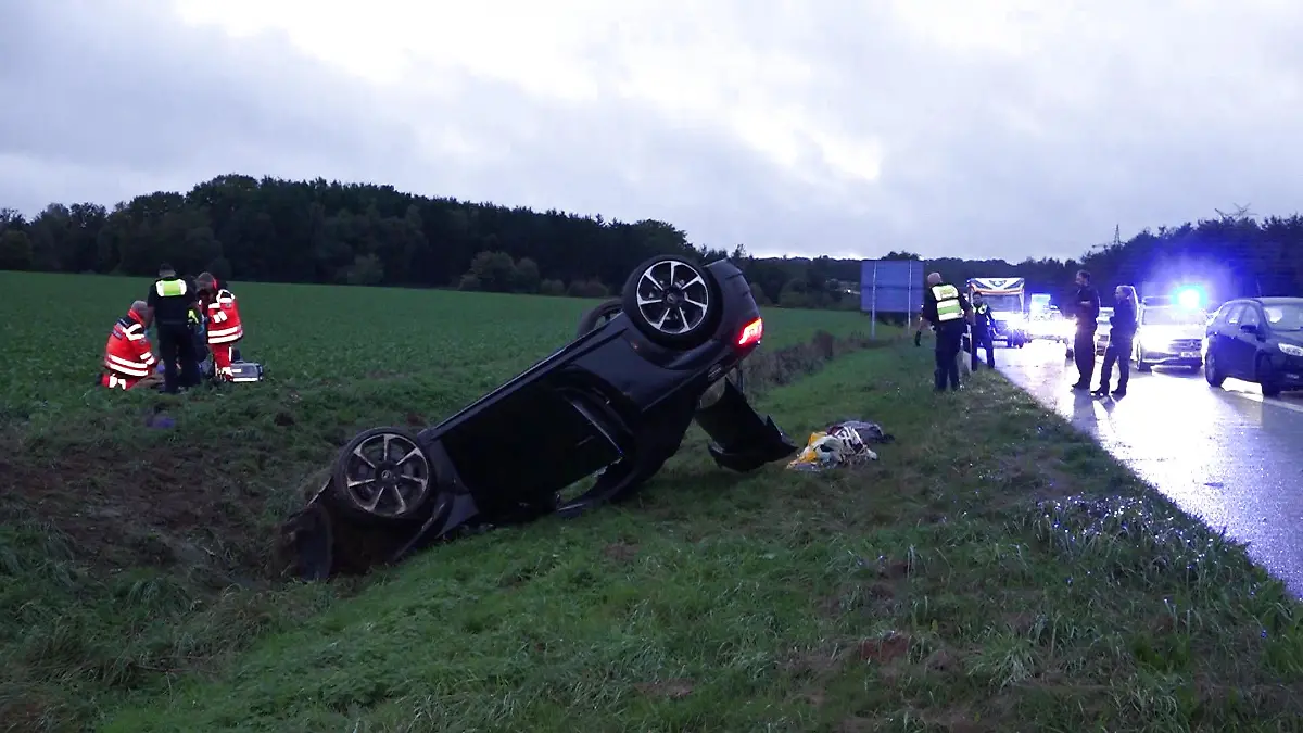 Ein überschlagenes schwarzes Auto neben einer Autobahn.