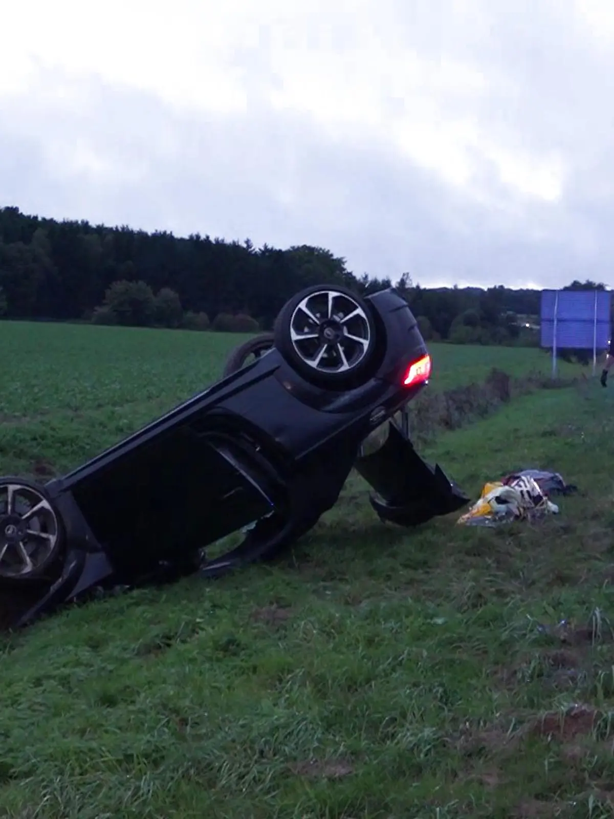 Ein überschlagenes schwarzes Auto neben einer Autobahn.