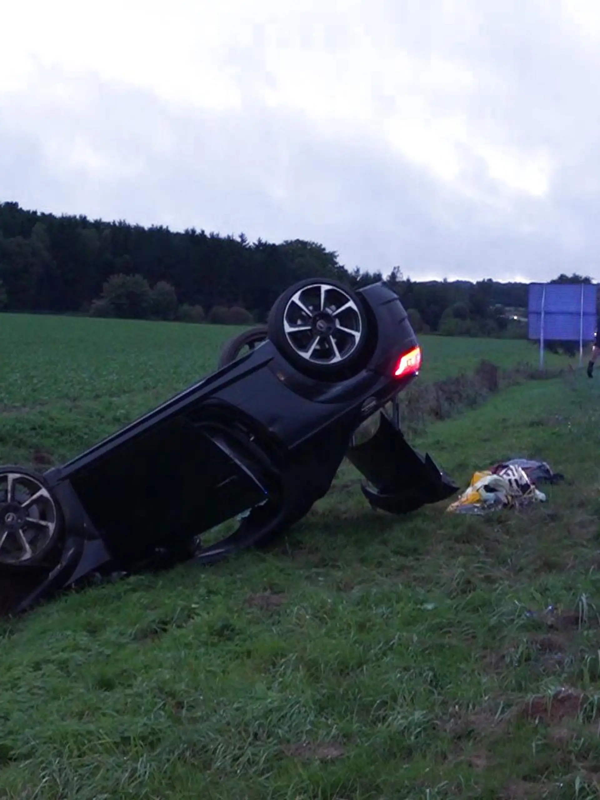 Ein überschlagenes schwarzes Auto neben einer Autobahn.