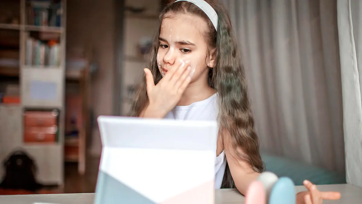 Beautiful teenage girl watching beauty master class with tablet online and doing spa procedure by herself, kid with smooth mask on face, beauty salon at home