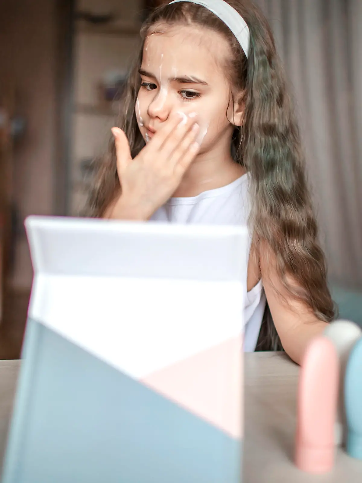 Beautiful teenage girl watching beauty master class with tablet online and doing spa procedure by herself, kid with smooth mask on face, beauty salon at home