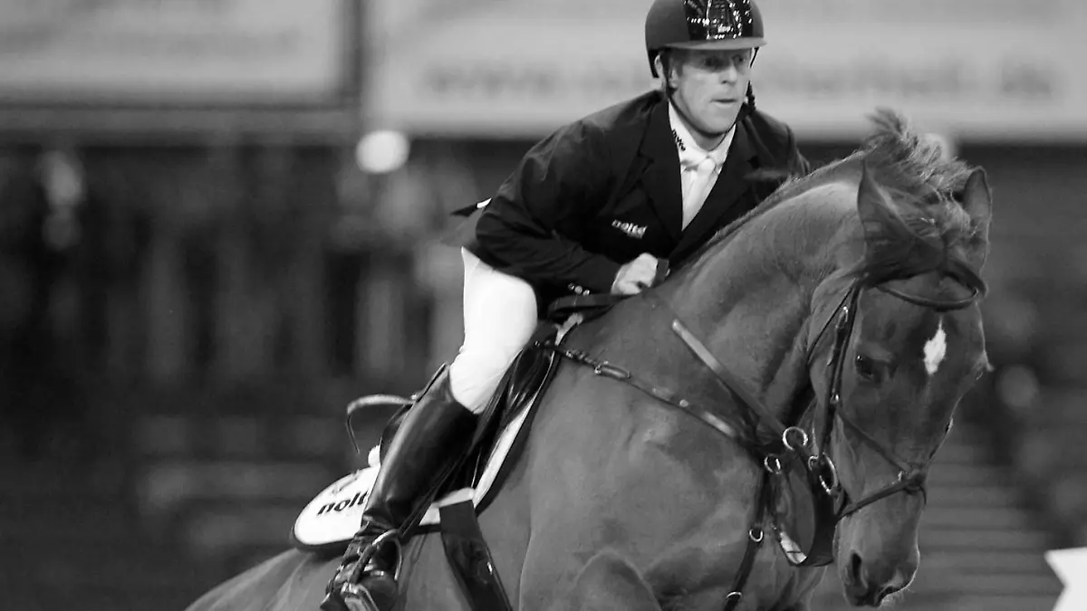 Ein Springreiter auf einem Pferd, das gerade eine Hürde überspringt.