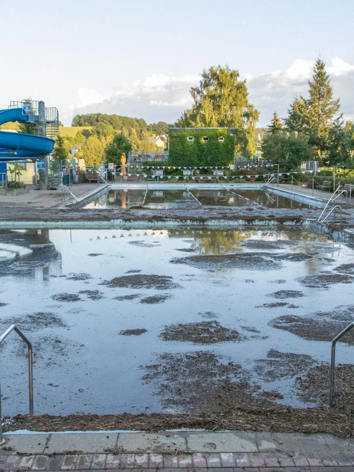 dpatopbilder - 06.09.2022, Sachsen, Burkhardtsdorf: Mit Schlamm ist ein Schwimmbecken in einem Freibad im Erzgebirge gefüllt. Nach Unwettern überrollte eine Schlammlawine das Freibad und spülte Schlamm und Geröll in die Schwimmerbecken. Die Freibad Saison ist hier für dieses Jahr beendet. Wie hoch der Schaden ist, kann mittlerweile noch nicht beziffert werden. Foto: André März/dpa +++ dpa-Bildfunk +++