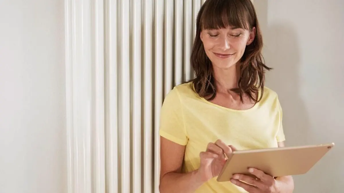 Eine junge Frau steht mit einem iPad vor einer Heizung