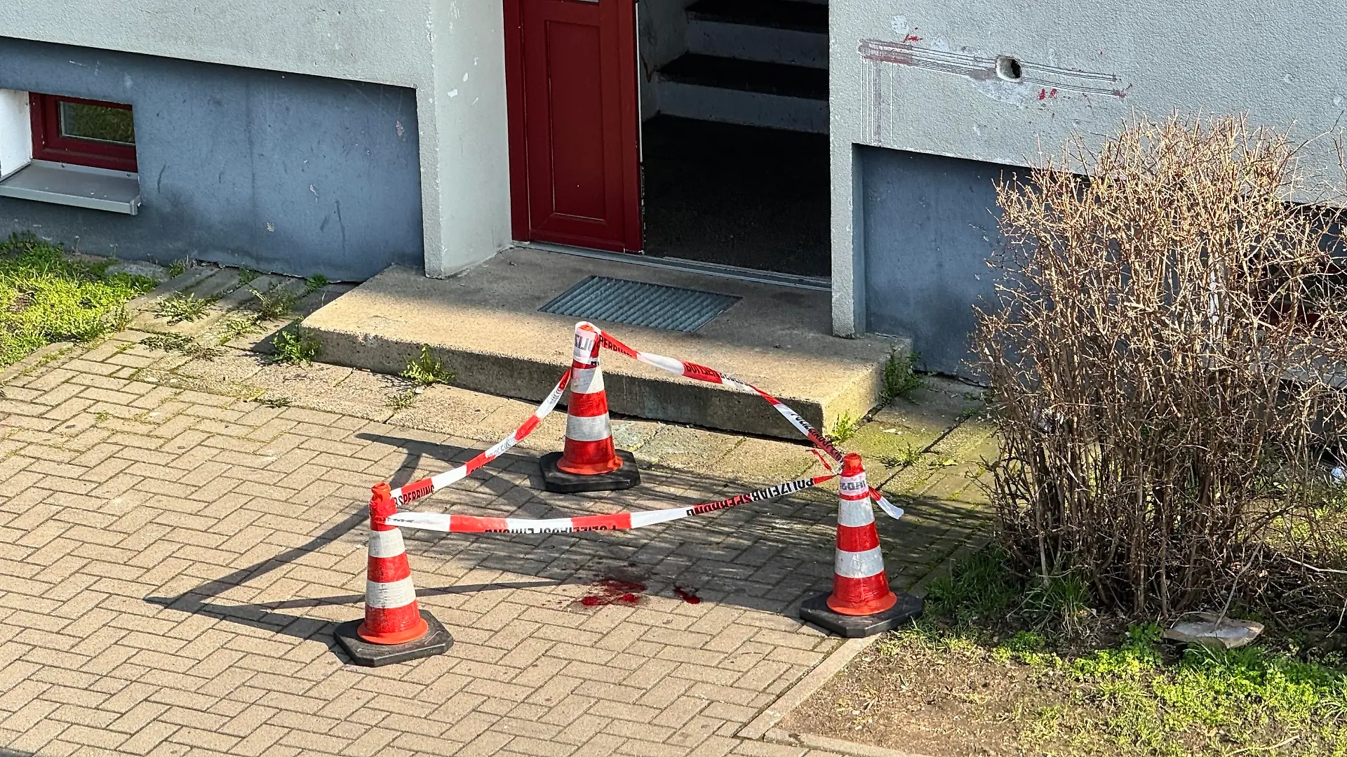 Polizisten haben in Magdeburg Blutspuren vor dem Eingang zu einem Haus mit Flatterband markiert.