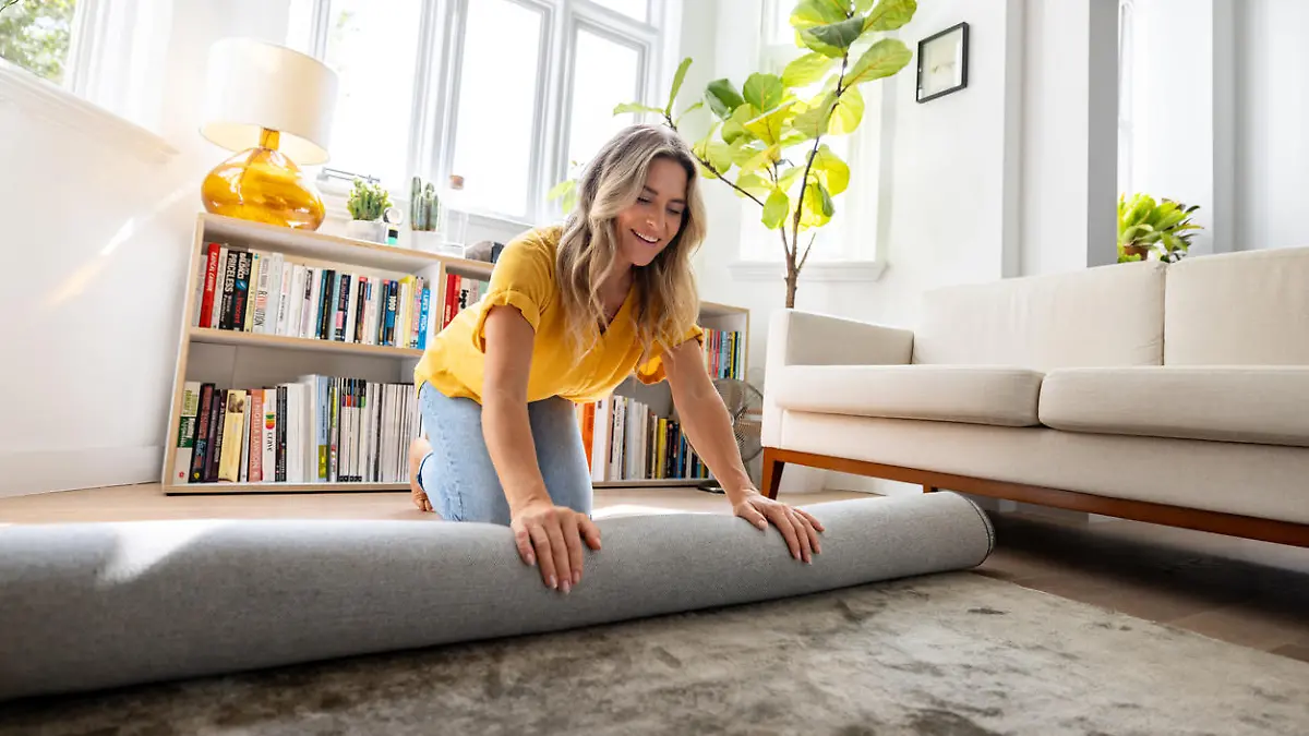 Happy Caucasian woman moving house and unrolling a carpet while unpacking - domestic life concepts