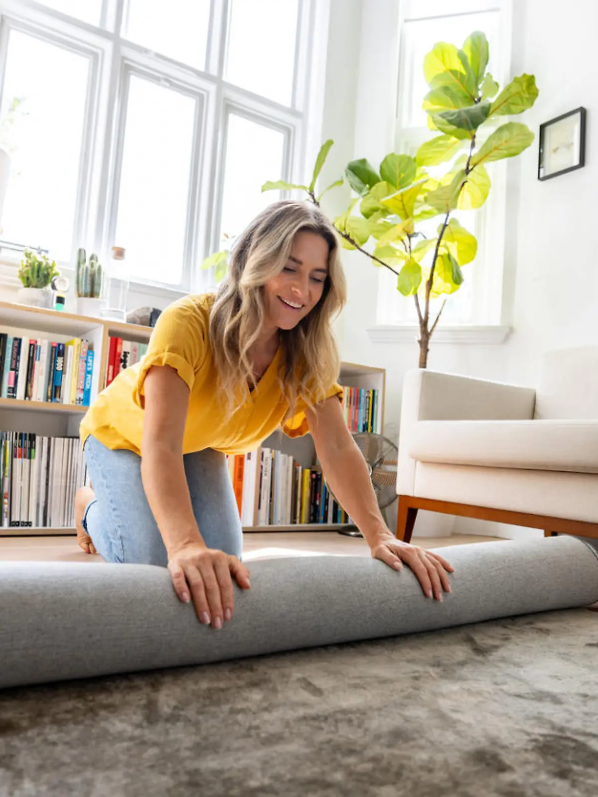 Happy Caucasian woman moving house and unrolling a carpet while unpacking - domestic life concepts