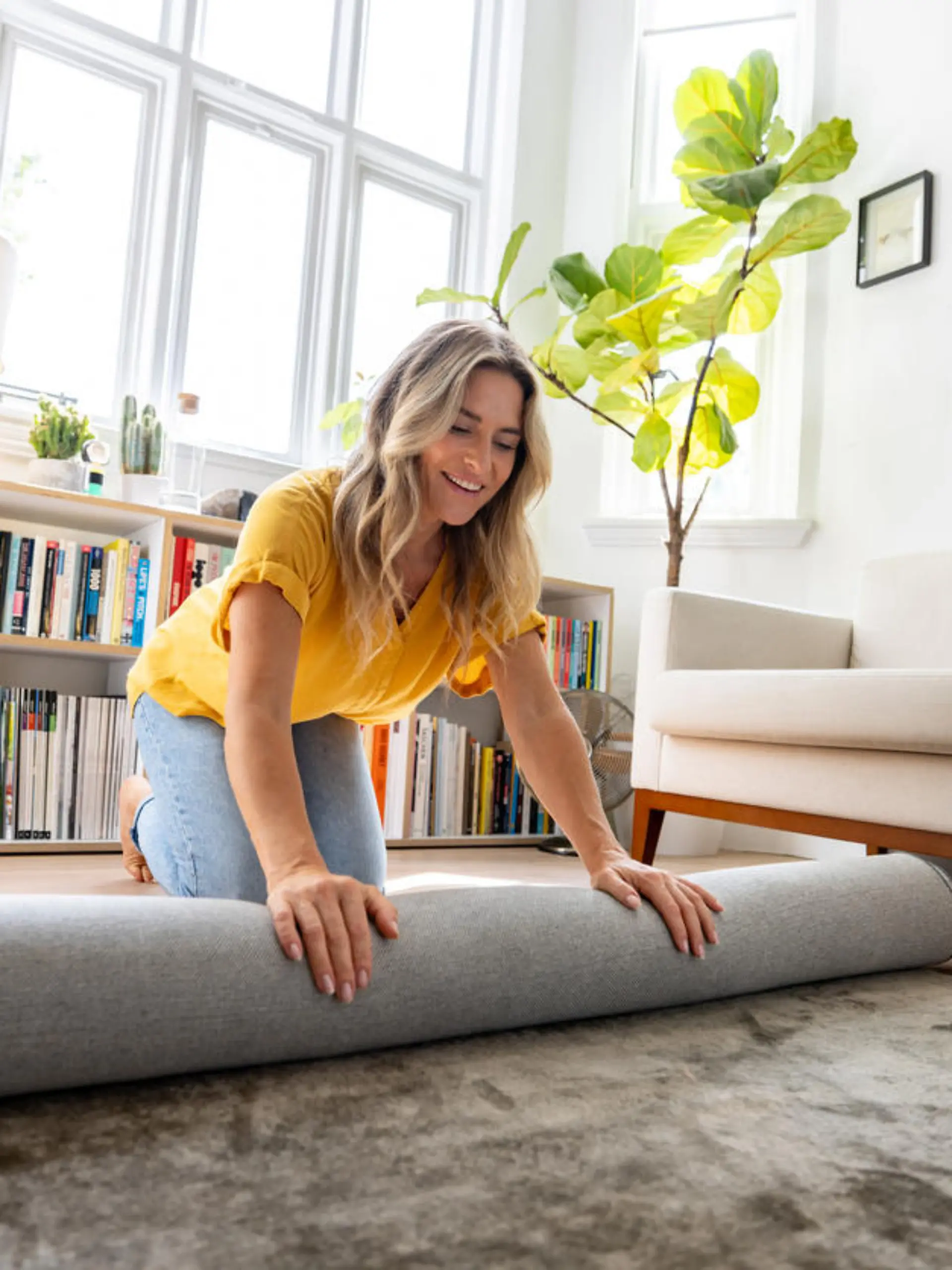 Happy Caucasian woman moving house and unrolling a carpet while unpacking - domestic life concepts