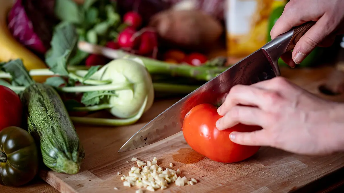 Eine Person schneidet auf einem Schneidbrett mit einem Küchenmesser eine Tomate.
