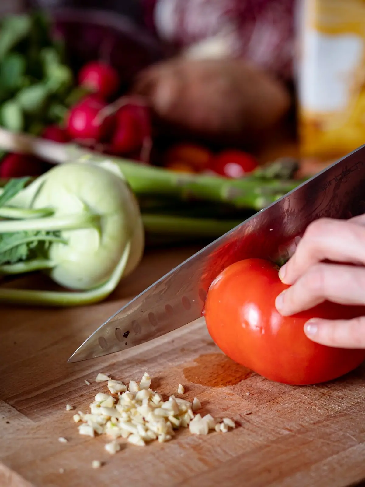 Eine Person schneidet auf einem Schneidbrett mit einem Küchenmesser eine Tomate.