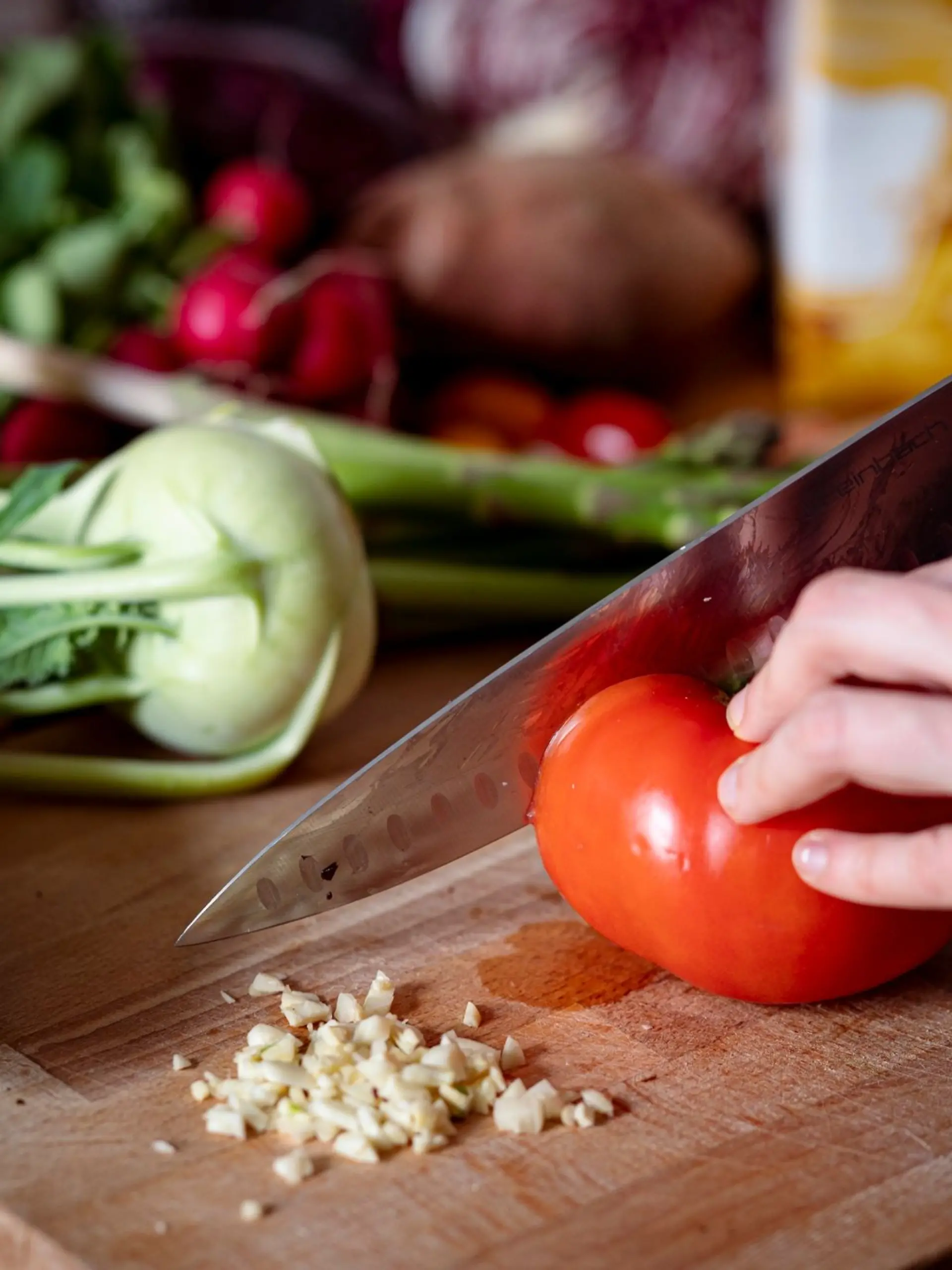 Eine Person schneidet auf einem Schneidbrett mit einem Küchenmesser eine Tomate.