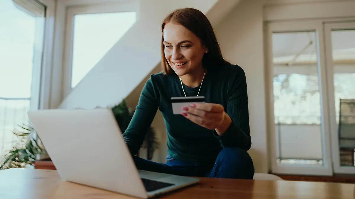 A smiling young woman sitting in the living room using a laptop to shop online and paying with a credit card