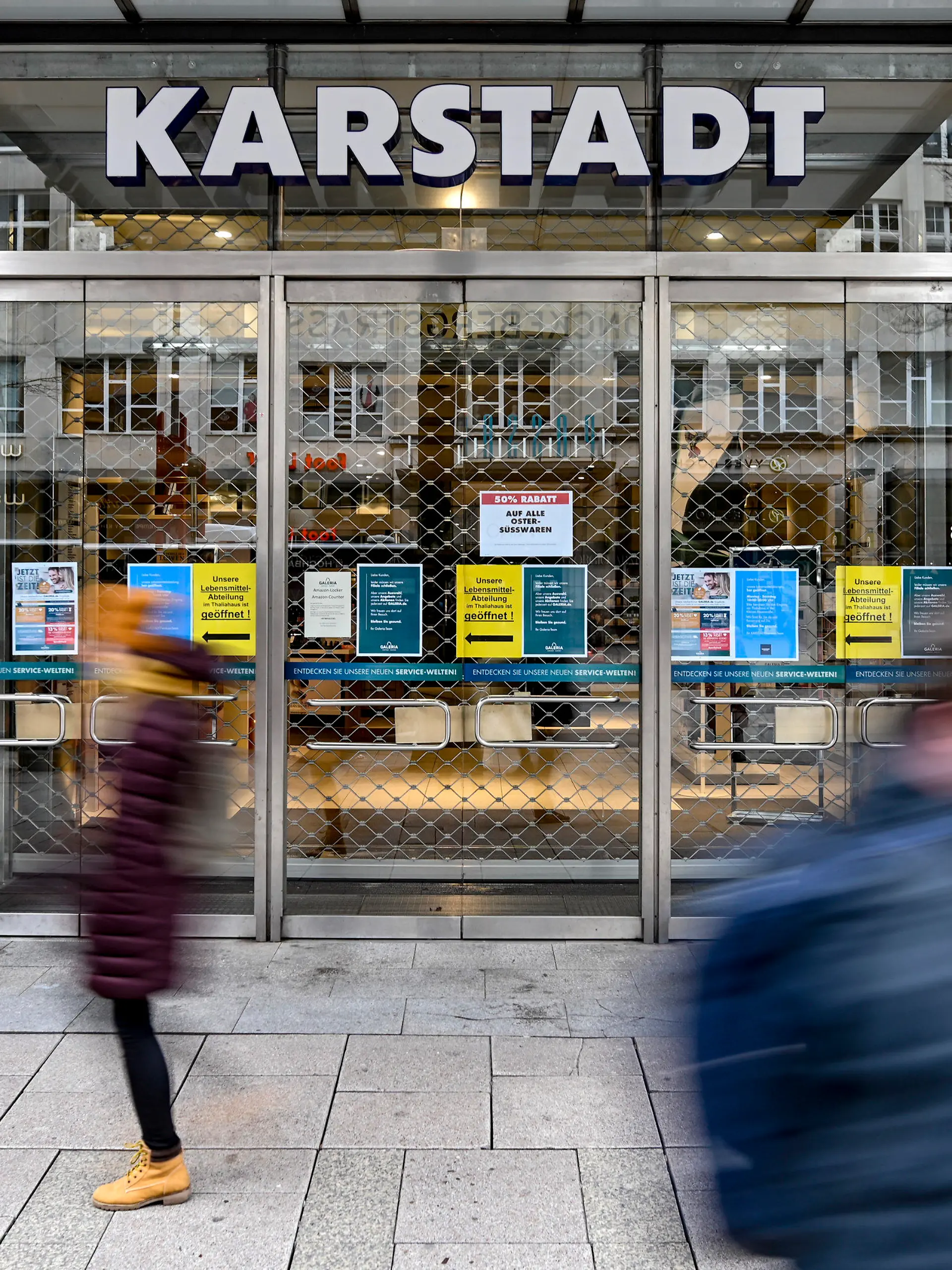 01.04.2020, Hamburg: Passanten laufern vor dem geschlossenen Eingang eines Kaufhauses der Warenhauskette Karstadt in der Innenstadt von Hamburg entlang. Die Warenhauskette Galeria Karstadt Kaufhof sucht angesichts der Umsatzeinbrüche durch die Corona-Pandemie Rettung in einem Schutzschirmverfahren. Dem Antrag des Unternehmens auf Einleitung des Verfahrens sei vom Amtsgericht Essen bereits stattgegeben worden, teilte der Konzern am 01.04.2020 mit. Das Schutzschirmverfahren schützt in die Krise geratene Unternehmen vor dem Zugriff der Gläubiger, ohne dass die Betriebe bereits Insolvenz anmelden müssen. Foto: Axel Heimken/dpa +++ dpa-Bildfunk +++
