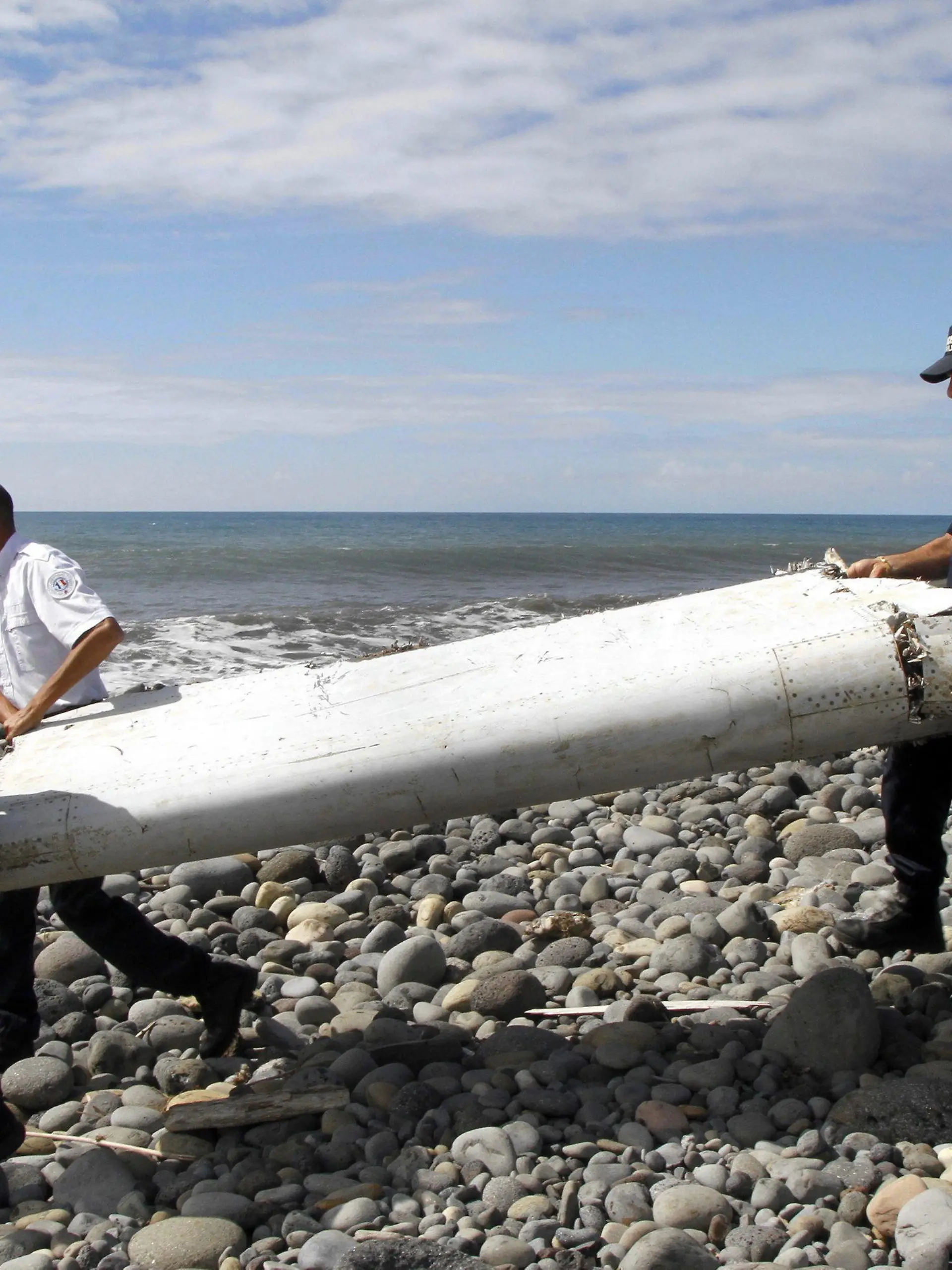 ARCHIV - 29.07.2015, Frankreich, La Reunion: Techniker tragen ein Wrackteil, die Flügelklappe eines Flugzeugs, über einen Strand bei Saint-Andre de la Reunion. An diesem Freitag jährt sich zum zehnten Mal das Verschwinden der Boeing-Maschine, mit 239 Menschen an Bord. (zu dpa: «Ein Mysterium seit zehn Jahren: Was geschah mit Flug MH370?») Foto: Raymond Wae Tion/MAXPPP/QUOTIDIEN DE LA REUNION/dpa +++ dpa-Bildfunk +++