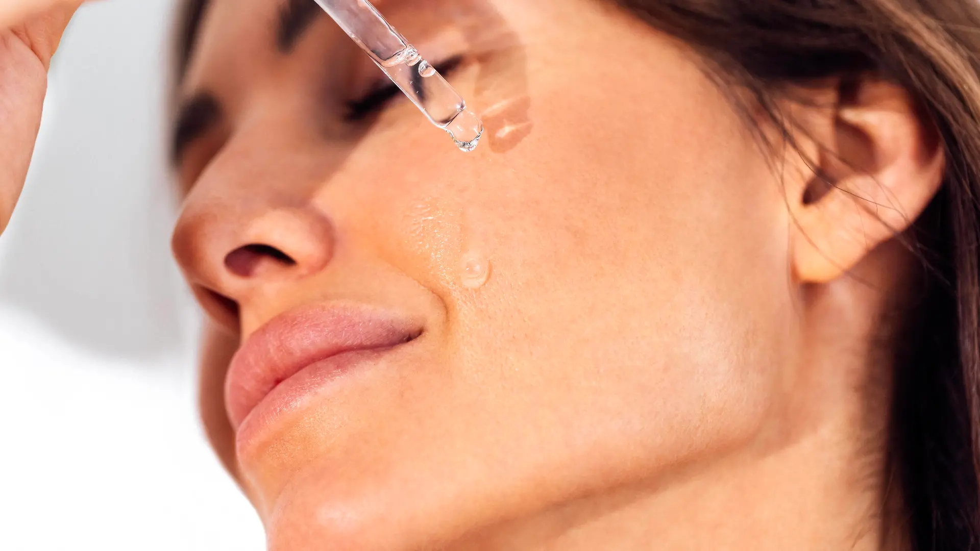 Young woman applies transparent serum from pipette to her face Extreme close up of beautiful smiling girl. Young woman applies transparent serum from pipette to her face. Pretty female brunette closed her eyes and relaxed during skin moisturizing procedure. ,model released, Symbolfoto Copyright: xZoonar.com/DashaxPetrenkox 20061492 ,model released, Symbolfoto ,property released
