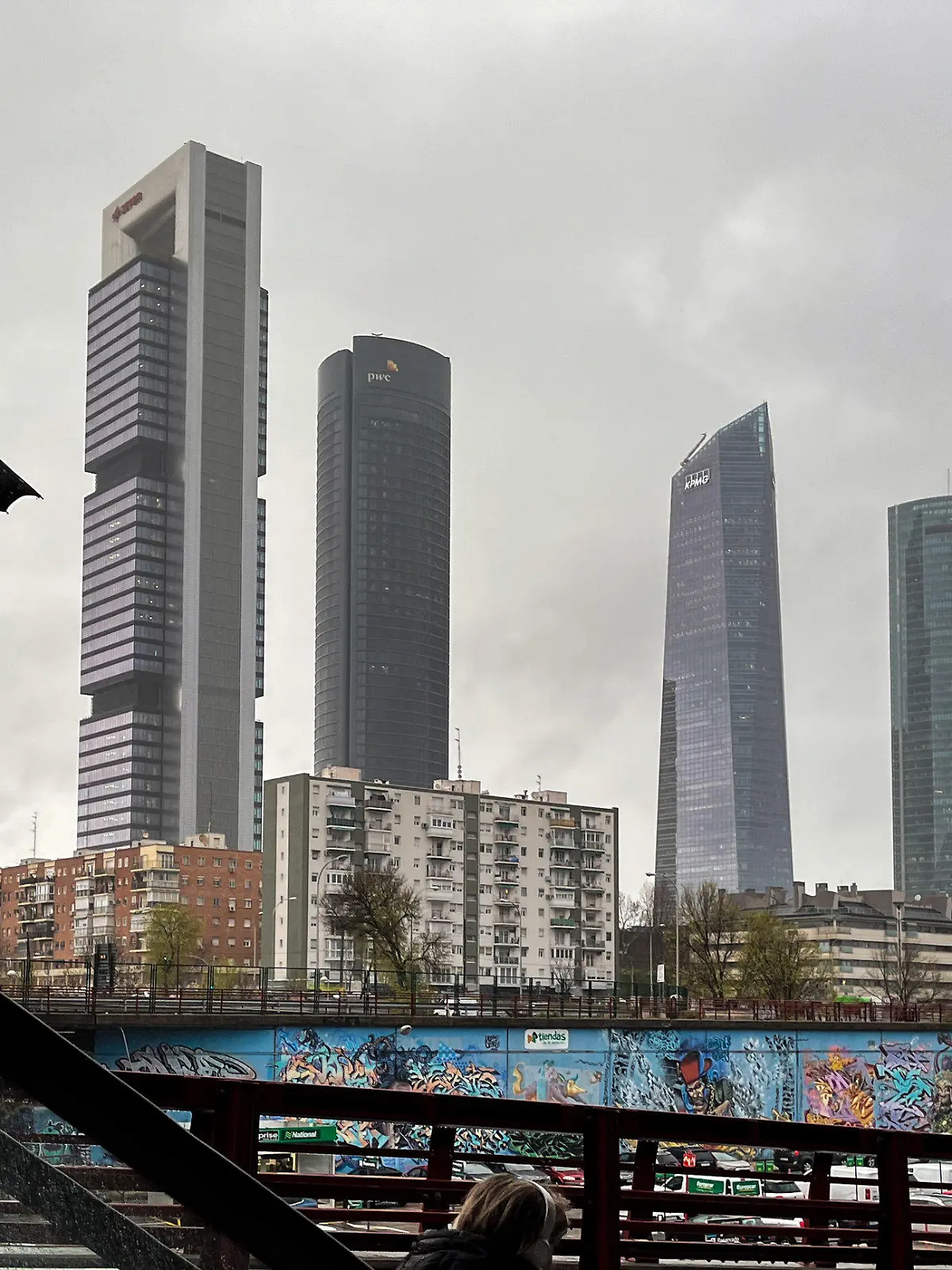 07.03.2024, Spanien, Madrid: Eine Frau mit Regenschirm fährt eine Rolltreppe vor der Kulisse der Cuatro Torres Business Area hinab. Die Meteorologen sagen auch für die nächsten Tage kühles und feuchtes Wetter für die Hauptstadt voraus. Foto: Jan Woitas/dpa +++ dpa-Bildfunk +++