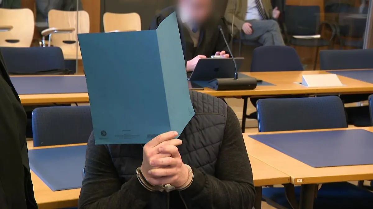 Beim Prozessauftakt verbirgt einer der Angeklagten sein Gesicht hinter einem Aktenordner.