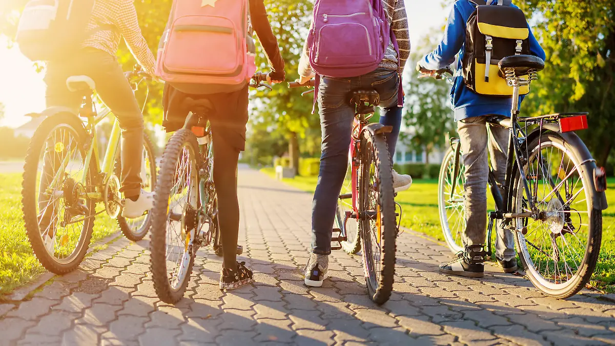 Children with rucksacks riding on bikes in the park near school. Pupils with backpacks outdoors