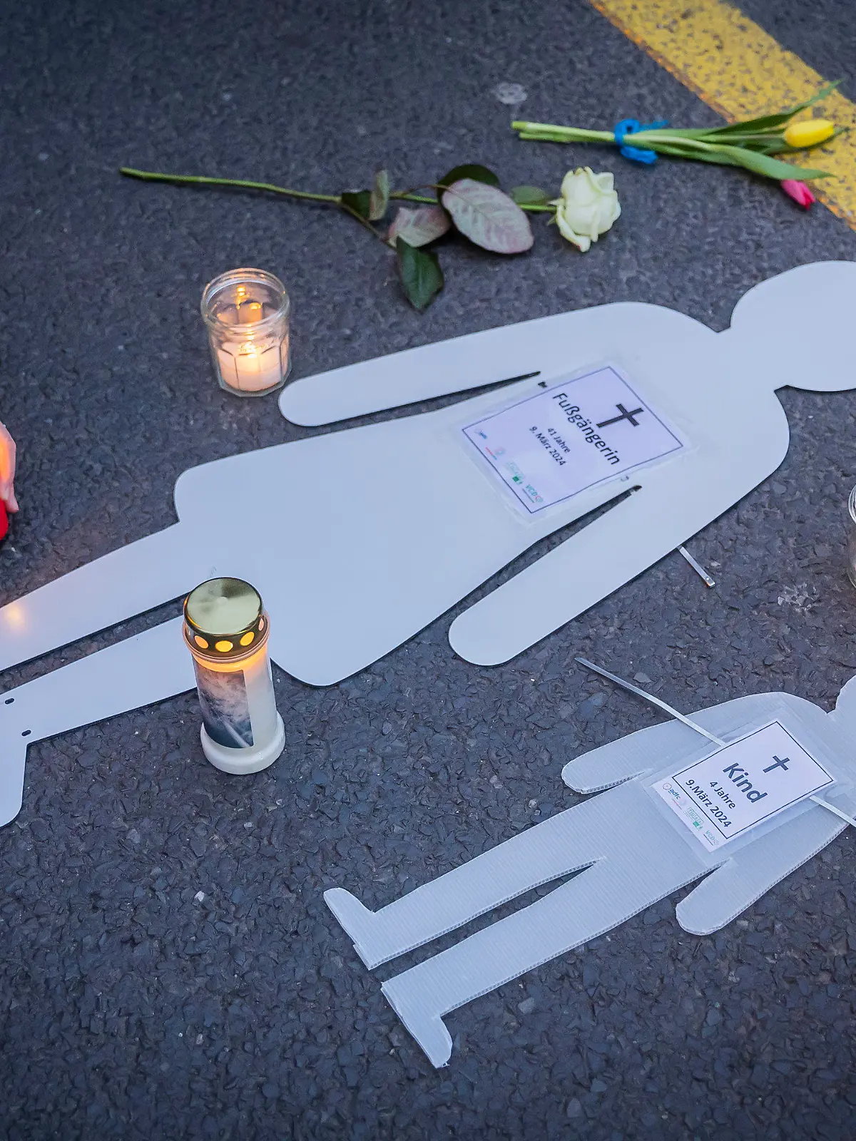 dpatopbilder - 10.03.2024, Berlin: Weiße Silhouetten einer Frau und eines Kindes liegen neben Blumen und Kerzen bei einer Mahnwache auf der Leipziger Straße. Bei einem schweren Verkehrsunfall am gestrigen Samstag (09.03.2024) erfasste nach Angaben der Berliner Polizei ein 83-jähriger Autofahrer eine 41-Jährige und ihren vierjährigen Sohn im Kinderwagen. Die Mutter starb kurz darauf im Krankenhaus, das Kind nach einer Notoperation noch am selben Abend. Zwei Angehörige wurden Zeugen des Unglücks. Foto: Christoph Soeder/dpa +++ dpa-Bildfunk +++
