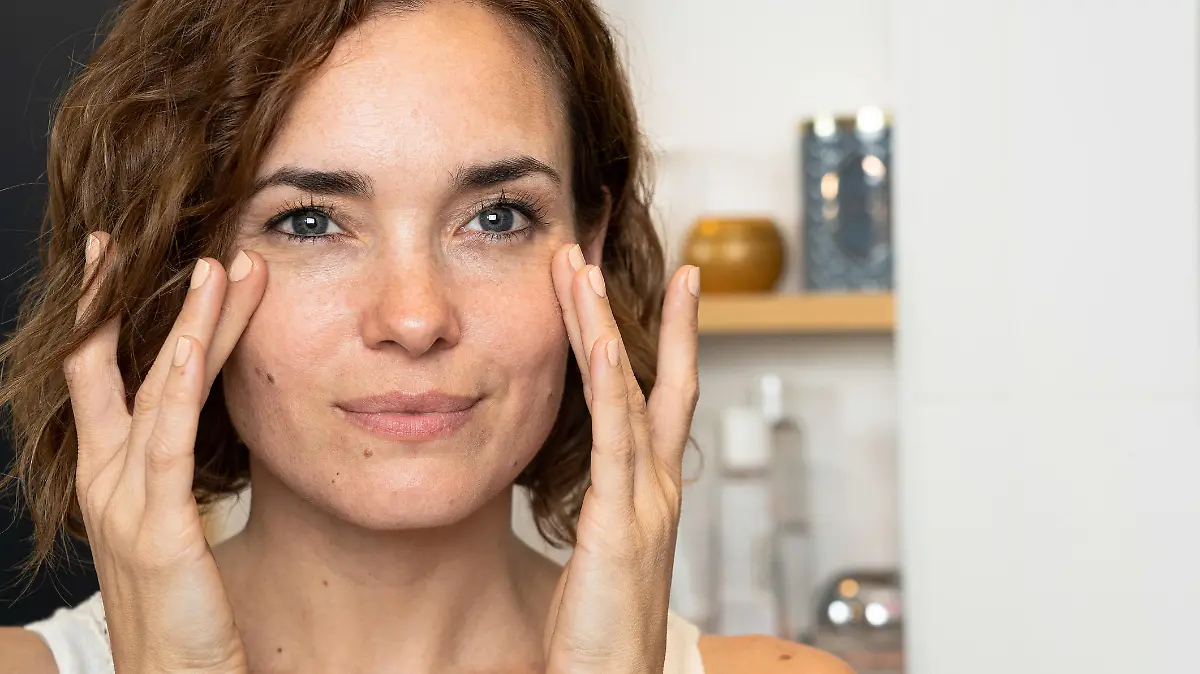 Smiling woman applying facial cream in the bathroom