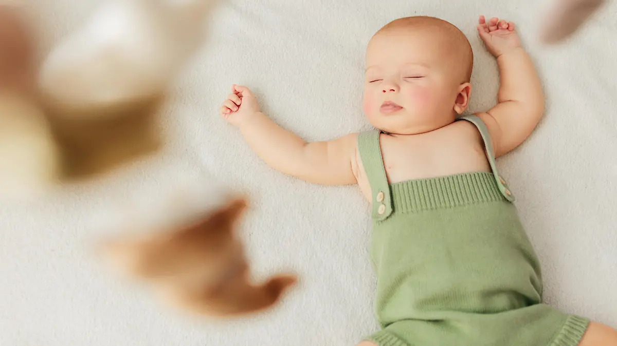 Little baby girl sleeps on a bed in a green suit, playmobile revolves over her.