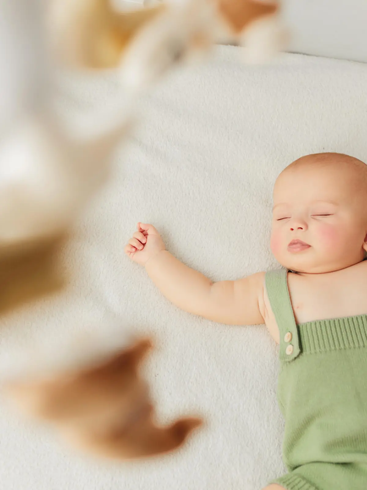 Little baby girl sleeps on a bed in a green suit, playmobile revolves over her.