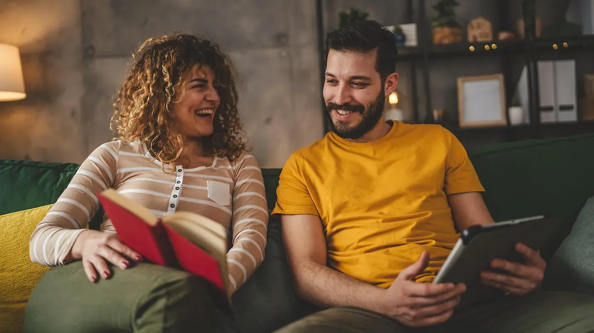 man and woman caucasian adult couple read book and use digital tablet at home on sofa bed