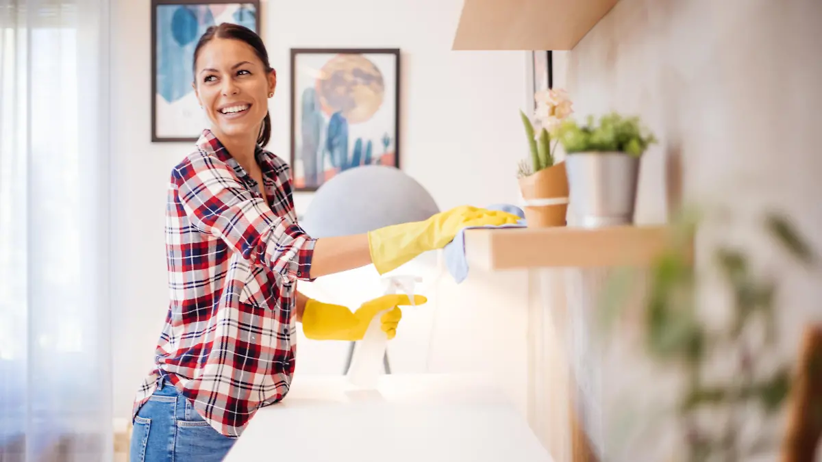 Beautiful Caucasian  young woman in casual clothes with yellow gloves cleaning furniture in living room at home.