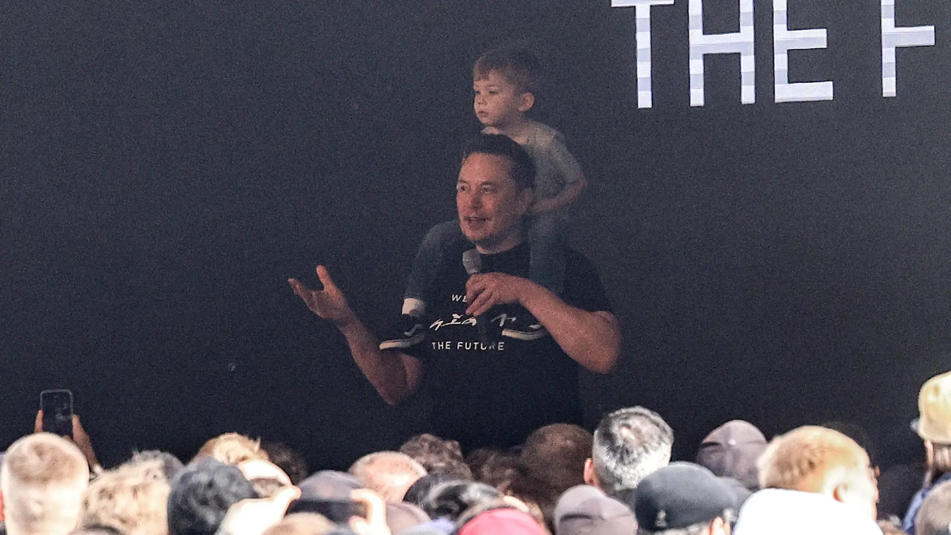 Tesla CEO Elon Musk enters the stage with a child on his shoulders at the Tesla Gigafactory for electric cars in Gruenheide near Berlin, Germany, Wednesday, March 13, 2024. Power has been restored to electric car manufacturer Tesla's factory near Berlin about a week after an outage believed to have been caused by arson, a network operator says. (AP Photo/Ebrahim Noroozi)