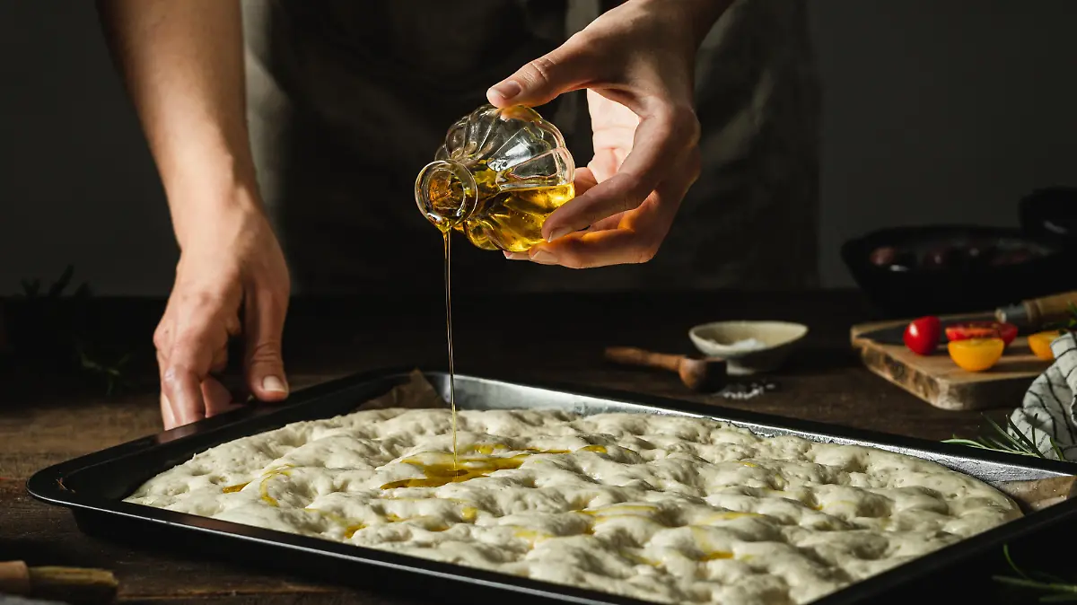 Mann beträufelt Foccacia mit Olivenöl.