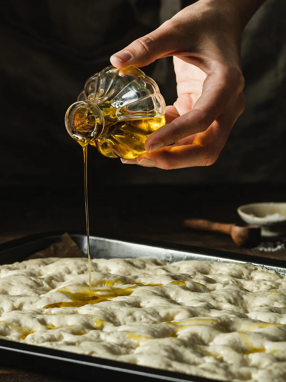Mann beträufelt Foccacia mit Olivenöl.