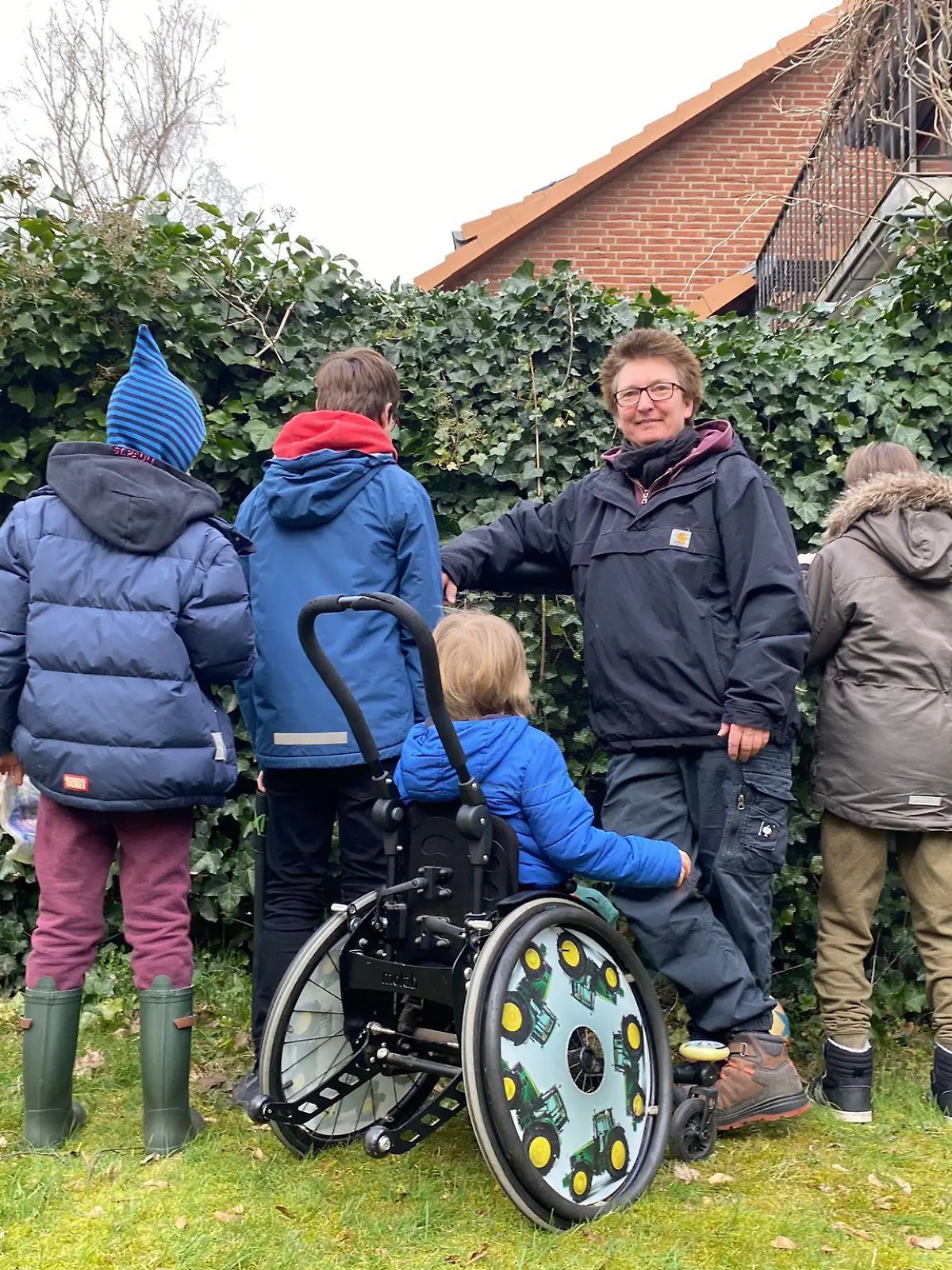 Eine Frau steht mit vier Kindern vor einem Busch
