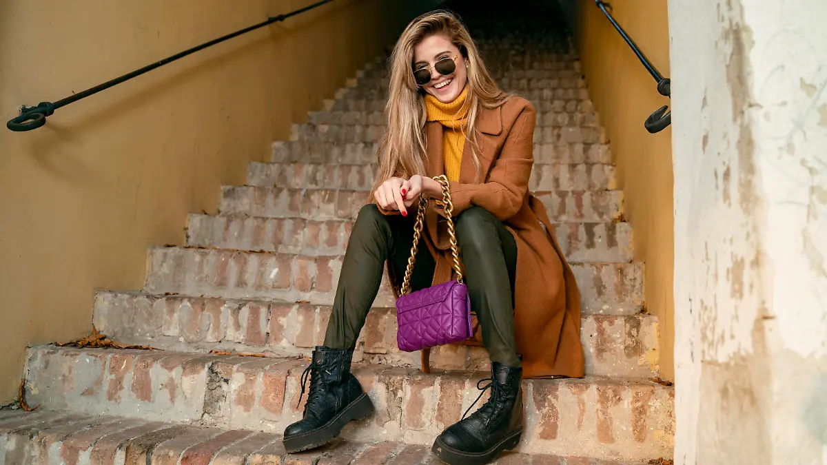 Blonde girl in coat sitting on the stairs and laughing, natural young woman
