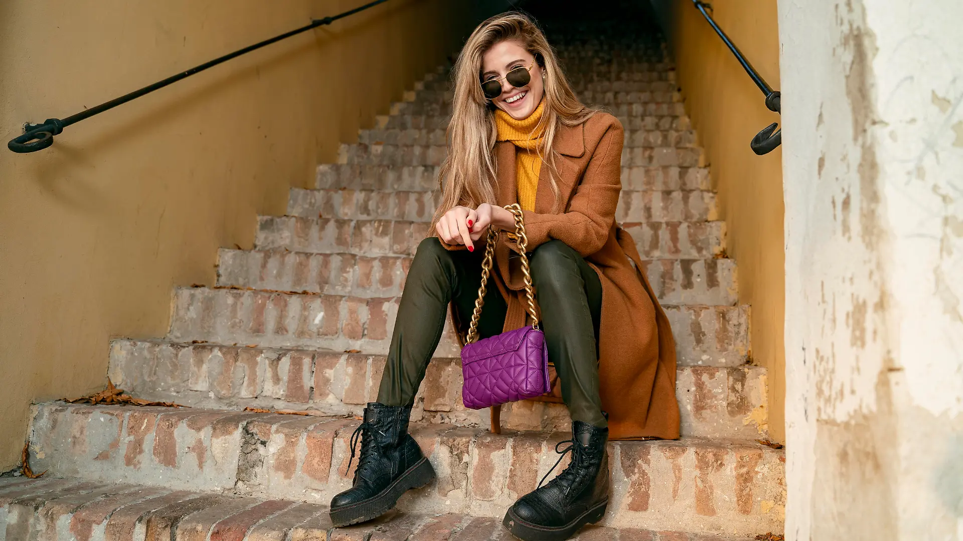 Blonde girl in coat sitting on the stairs and laughing, natural young woman