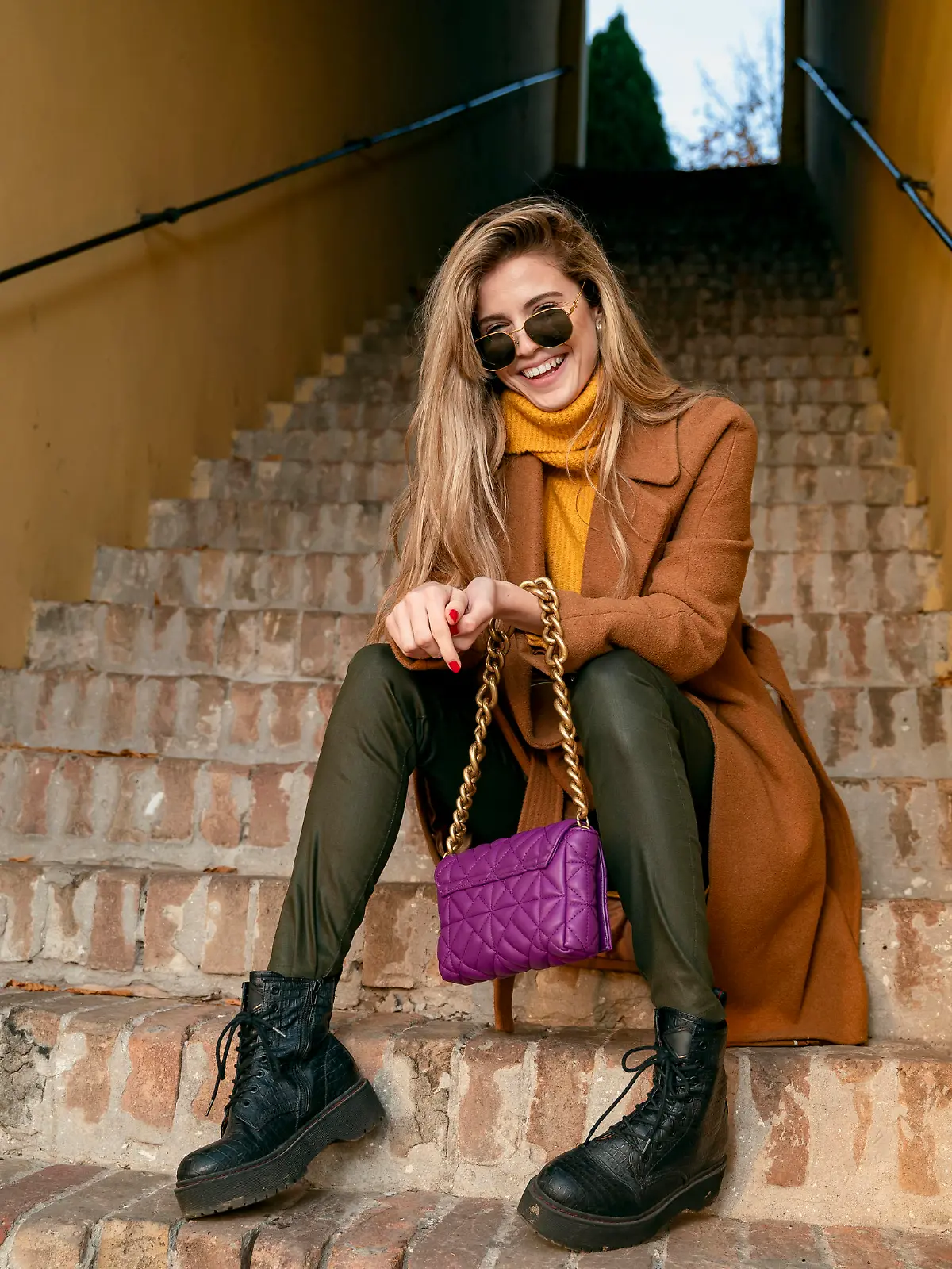 Blonde girl in coat sitting on the stairs and laughing, natural young woman