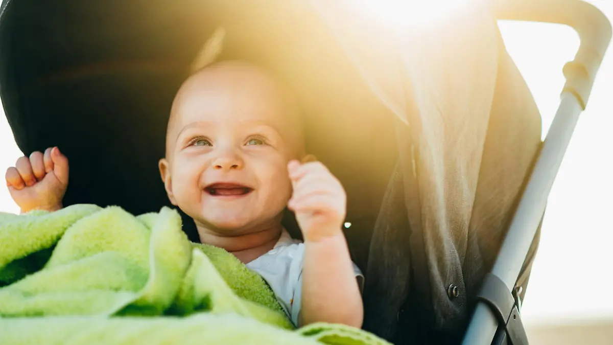 Portrait of a happy baby boy sitting in a baby stroller on the beach on a summer vacation. Baby protected from the sun. Tropical vacation.