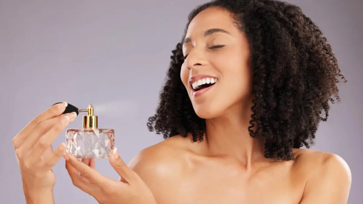 Beauty, luxury and female in a studio with perfume for a fresh scent, bodycare or wellness. Happy, smile and woman model with bottle of fragrance for cosmetic health isolated by a gray background.