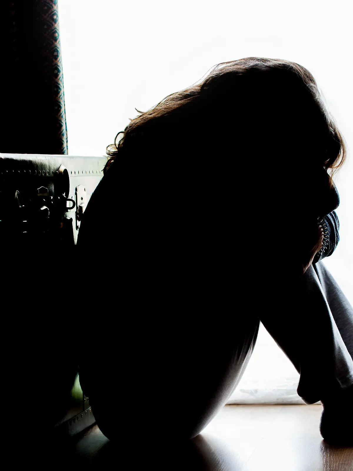 Unhappy mature lady, woman in silhouette, sitting on the floor with back lit. Depressing thoughts. || Modellfreigabe vorhanden