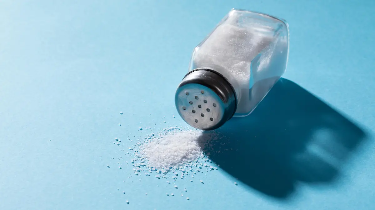 High angle close-up of salt spilling from salt shaker on blue background with copy space. unaltered, ingredient, food, shadow, rock salt and seasoning.
