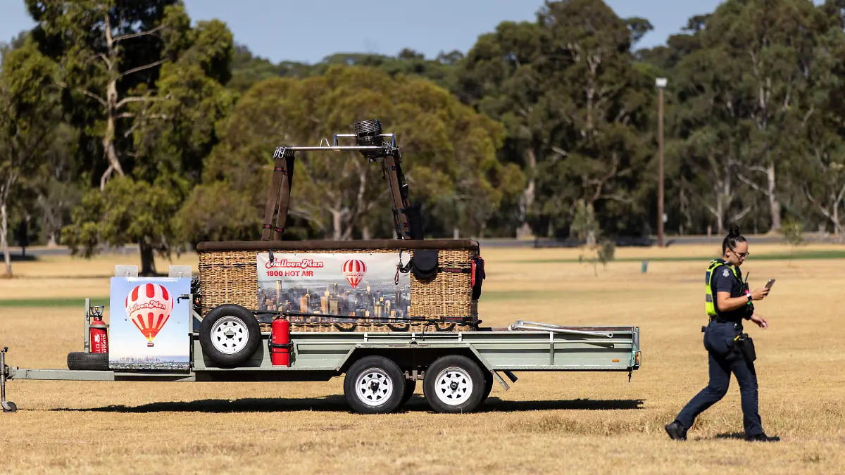 A police officer walks past a trailer with a hot-air balloon basket on it after the discovery of a man's body at Yarra Bend Park in Melbourne, Monday, March 18, 2024. A man has fallen to his death from a hot-air balloon as it passed over suburban Melbourne, Australia's second largest city. (Diego Fedele/AAP Image via AP)