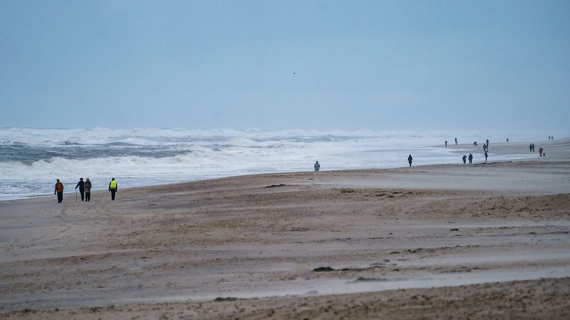 ARCHIV - 30.11.2021, Schleswig-Holstein, Westerland/Sylt: Spaziergänger gehen am Strand von Westerland entlang, an dem sich durch starke Sturmböen das Wasser zu hohen Wellen auftürmt. Sturm und Wellen tragen jedes Jahr etliche Kubikmeter Sand vor den Küsten der Insel ab. Bei der sogenannten Strandbereisung wollen Experten am Montag (18. März) prüfen, wie viel Sand in diesem Jahr vor die Küste (zu dpa: «Experten wollen Strände nach Winterstürmen auf Sylt prüfen») Foto: Axel Heimken/dpa +++ dpa-Bildfunk +++